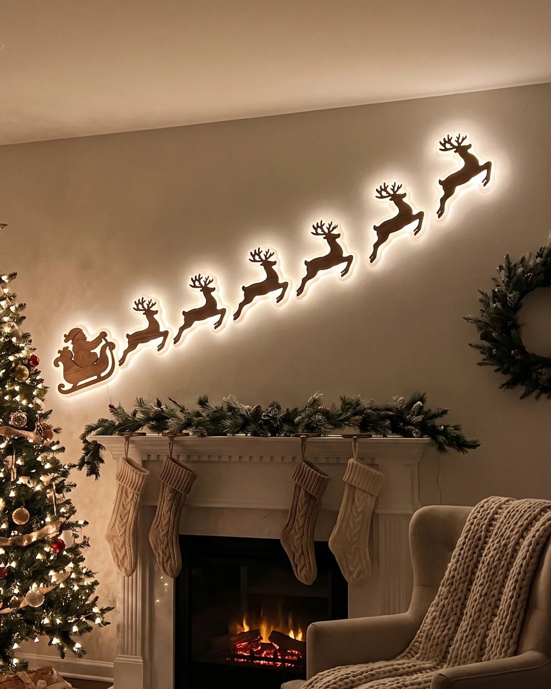 Santa's sleigh and six reindeer glowing warm white on the wall above a cozy fireplace